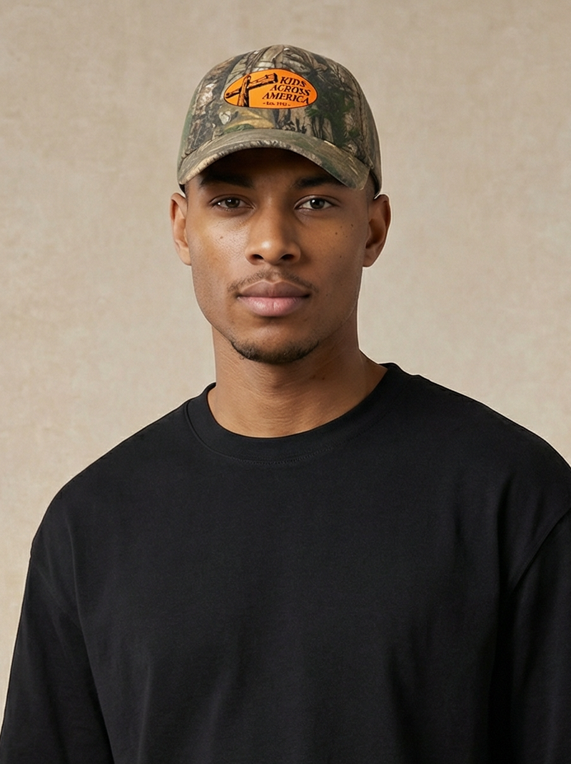 Man wearing a black t-shirt and pants with a cap, standing against a beige background